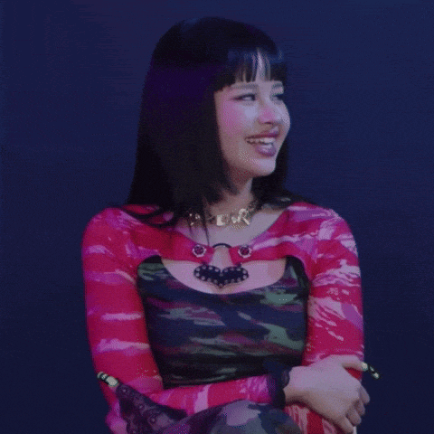a woman wearing a necklace and a pink top smiles