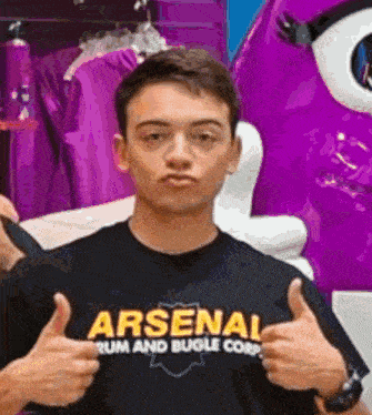 a young man wearing a black shirt that says arsenal rum and bugle corp giving a thumbs up