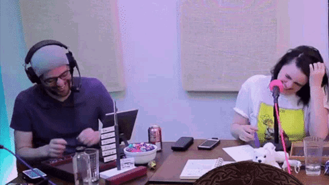 a man and a woman are sitting at a table with a microphone and a bowl of candy .
