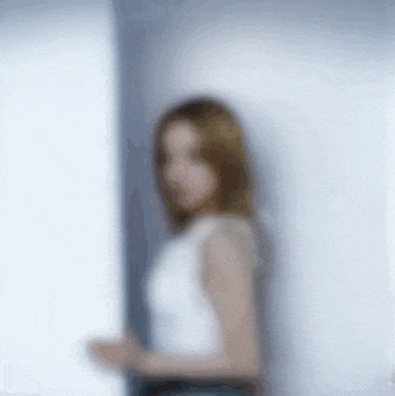 a blurry picture of a woman in a white tank top standing next to a window .
