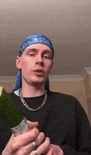 a man wearing a blue bandana and a necklace holds a bottle