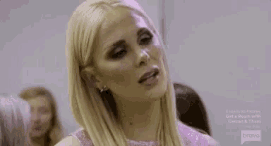 a blonde woman is wearing a pink dress and earrings and looking at the camera .