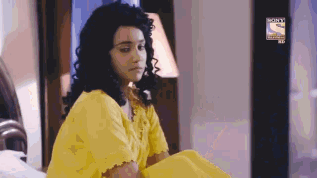a woman in a yellow dress sits on a bed in front of a sign that says sony television