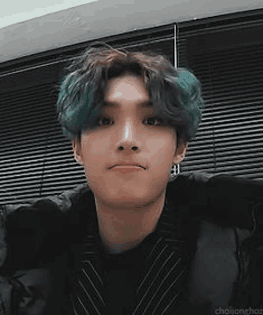 a young man with green hair is looking at the camera while wearing a black jacket .