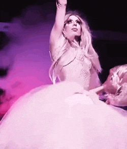 a woman in a white dress is dancing on a stage in front of a purple background .