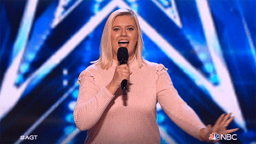 a woman in a pink sweater is singing into a microphone on nbc