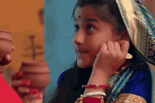 a little girl with a scarf around her head is looking at herself in the mirror