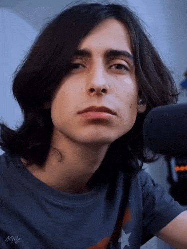a young man with long hair is wearing a gray shirt with a star on it .