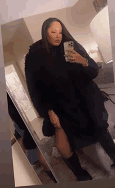 a woman in a black coat is taking a selfie in front of a mirror
