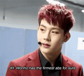 a young man with red hair is talking into a microphone while wearing a red suit and black shirt .