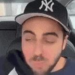 a man with a beard wearing a ny yankees hat is sitting in the back seat of a car .