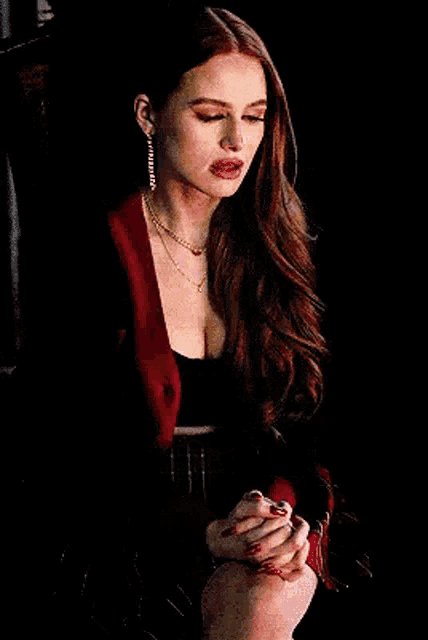 a woman with long red hair is wearing a red jacket and black top .