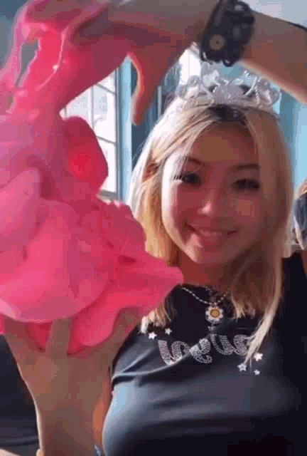 a girl wearing a tiara and a black shirt is holding a pink object .