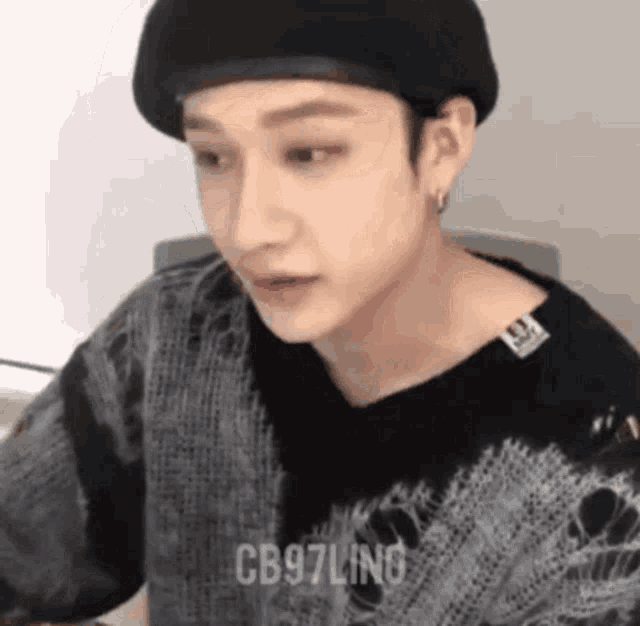 a young man wearing a black beret and a black sweater is sitting at a table .