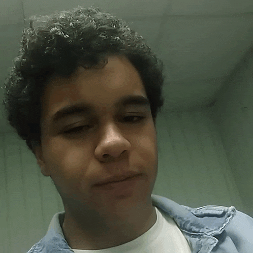 a young man with curly hair is wearing a white shirt and blue jacket