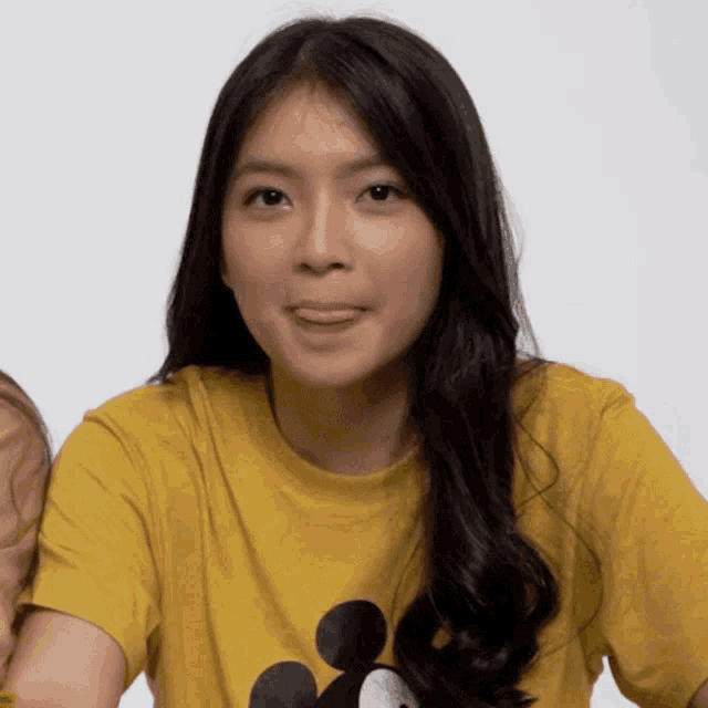 a woman wearing a yellow shirt with mickey mouse on it sticks out her tongue