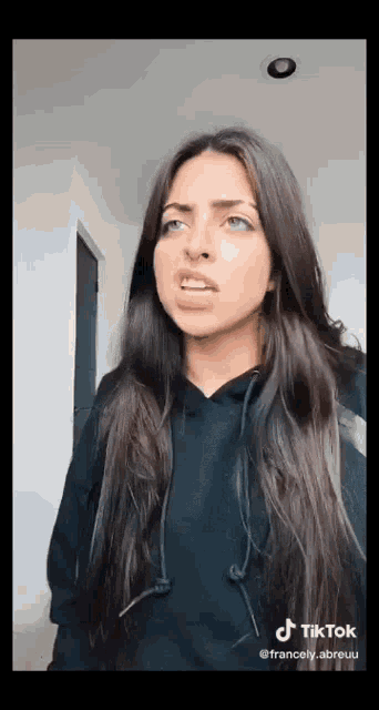 a woman with long dark hair is making a funny face while wearing a black hoodie .