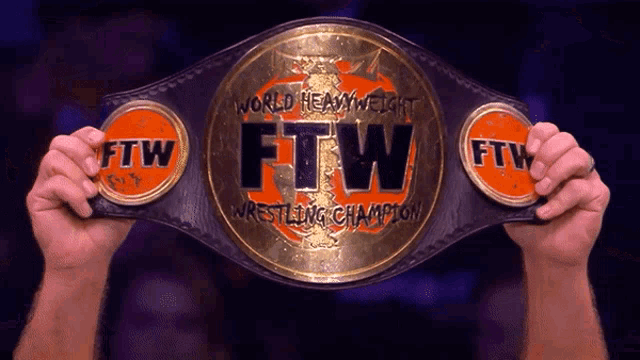 a person is holding up a world heavyweight ftw wrestling champion belt