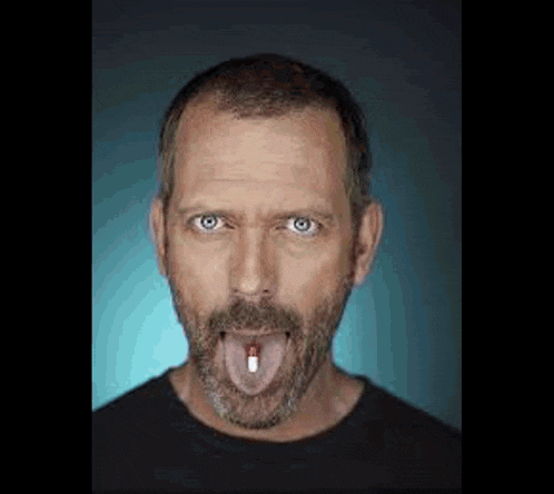 a man with a beard is sticking out his tongue and holding a pill in his mouth .