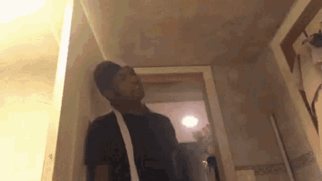 a man in a black shirt is standing in a hallway with a white strap around his shoulder .