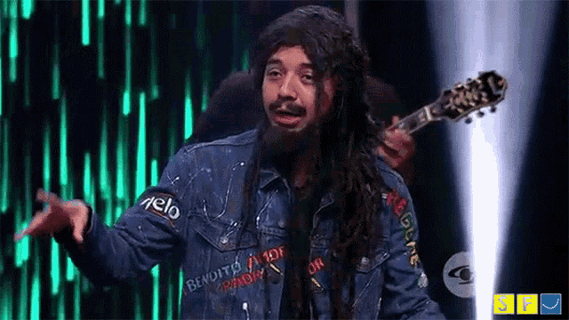 a man with long dreadlocks is holding a guitar and wearing a denim jacket with bendito written on it