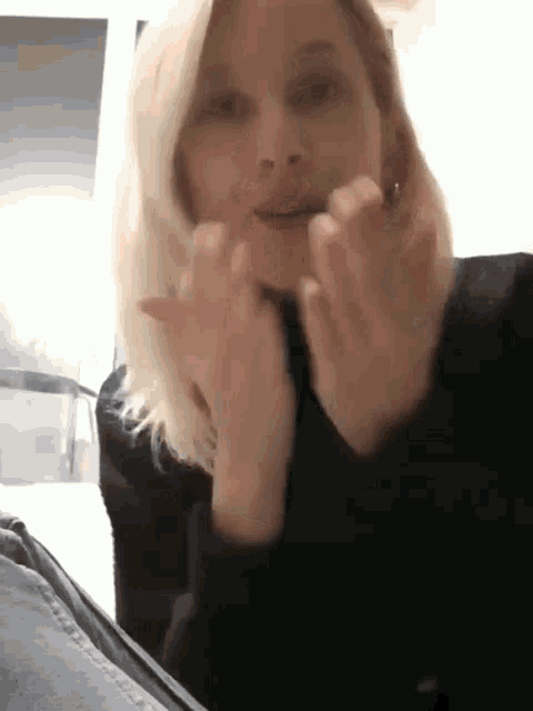 a woman with blonde hair is wearing a black sweater and making a funny face