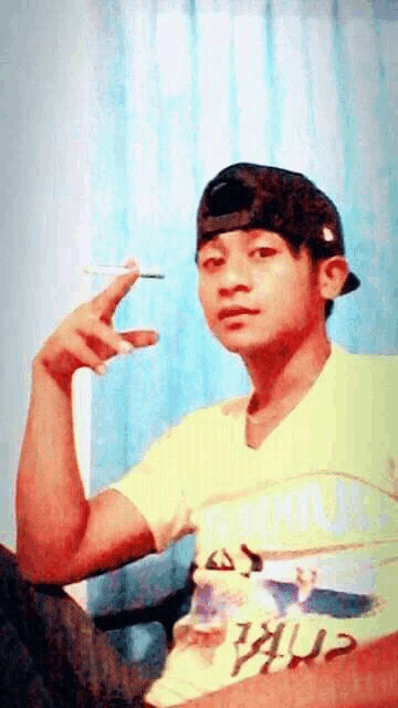 a young man wearing a hat and a yellow shirt is smoking a cigarette