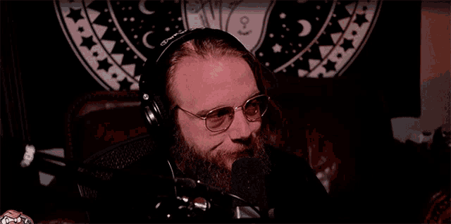 a man with a beard wearing headphones and glasses is sitting in front of a microphone