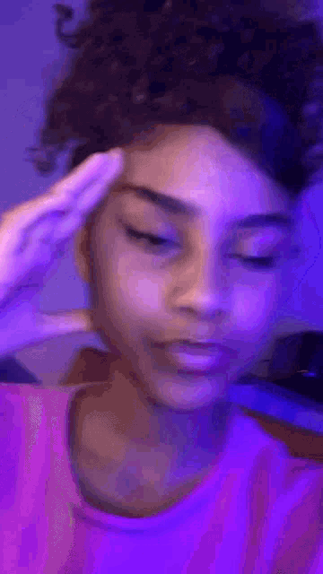 a girl with curly hair is making a funny face while wearing a purple shirt and a headband .