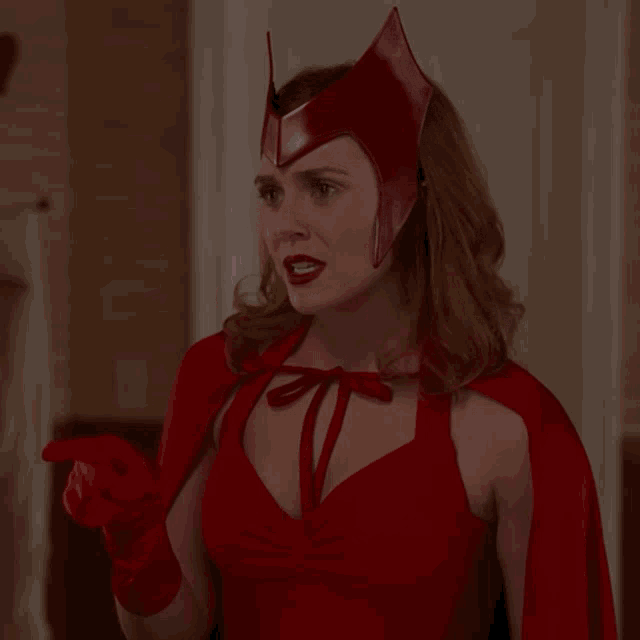 a woman in a red dress and cape is pointing her finger
