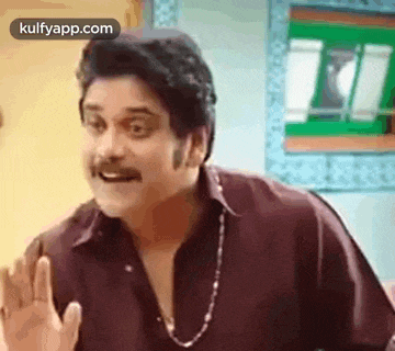 a man with a mustache is making a funny face while wearing a maroon shirt and a necklace .