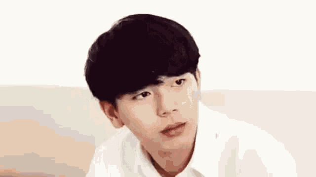 a young man with black hair and a white shirt is sitting on a couch looking at the camera .