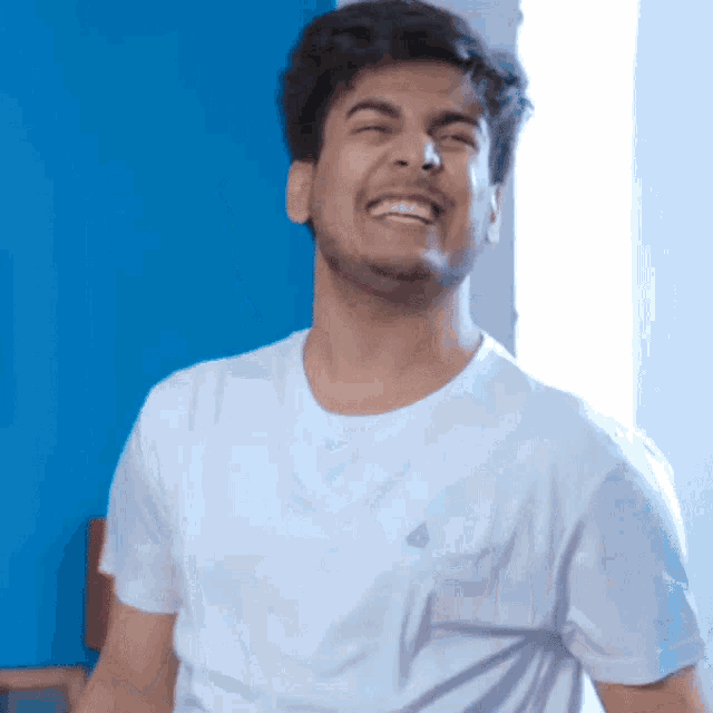 a man in a white t-shirt is laughing with his mouth open
