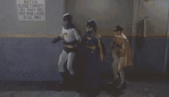 a batman and batgirl are standing next to each other in front of a sign that says keep door locked at all times .