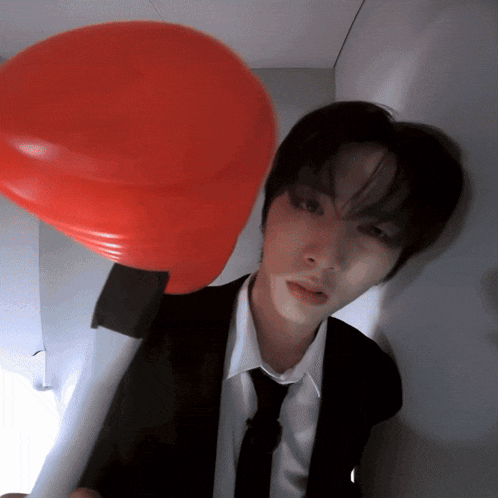 a man in a suit and tie holds a red balloon in front of his face