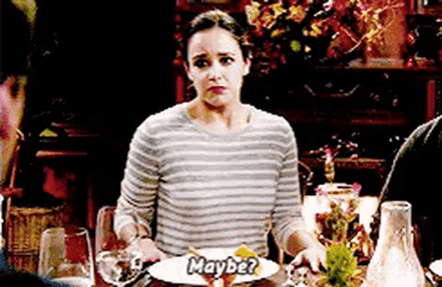a woman is sitting at a dinner table with a plate of food and a glass of wine .