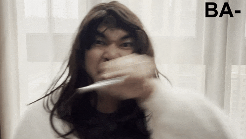 a man with long hair is brushing his teeth in front of a white curtain with ba written on it