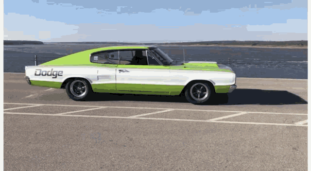 a green and white dodge car is parked on the side of a road
