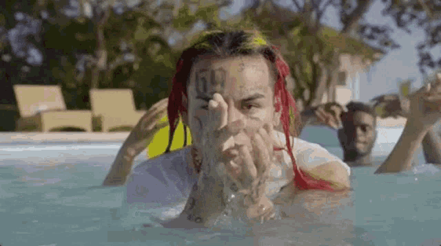 a man with dreadlocks is laying in a swimming pool with his hands on his face .
