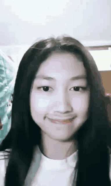 a young girl with long black hair and a white shirt is smiling .