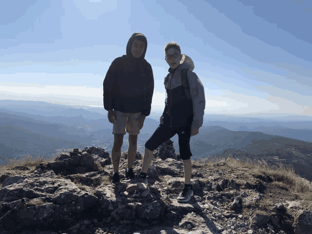 a man and a woman standing on top of a rocky mountain