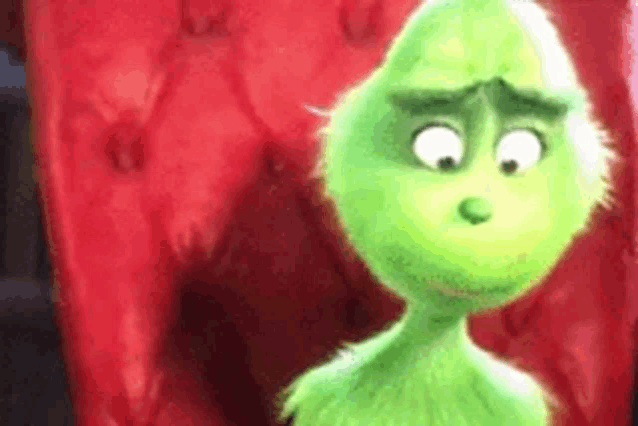a close up of a green cartoon character standing in front of a red couch .