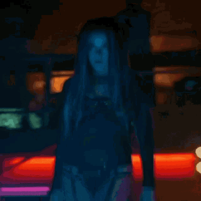 a woman with long blue hair is standing in front of a red car in a dark room .