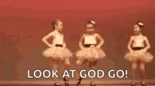 two little girls in tutus are dancing on a stage and they are looking at god go .