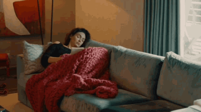 a woman laying on a couch with a red blanket on her