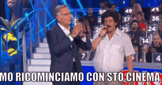 a man in a wig sings into a microphone with the words mo ricominciamo con sto cinema below him