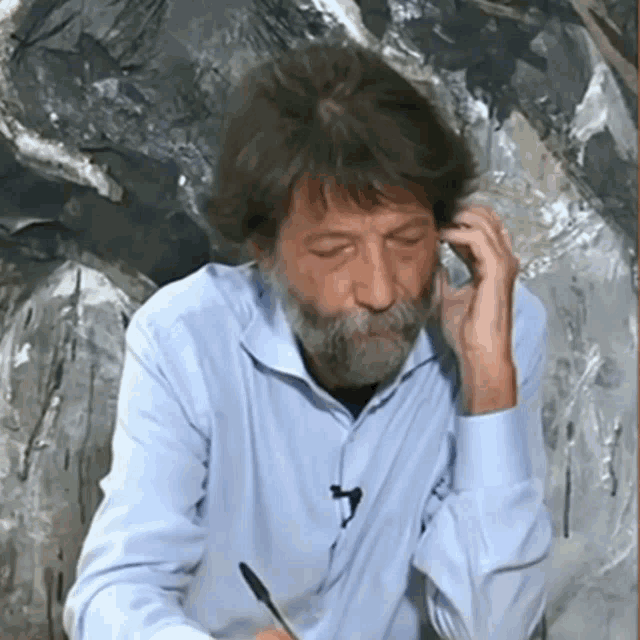 a man with a beard wearing a blue shirt talks on a cell phone