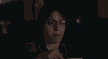 a woman wearing glasses is sitting in a dark room using a tablet computer .