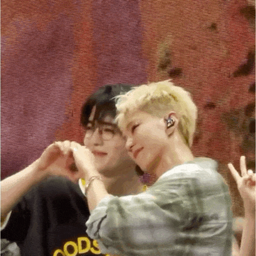 a couple of men are making a heart shape with their hands while standing next to each other on a stage .