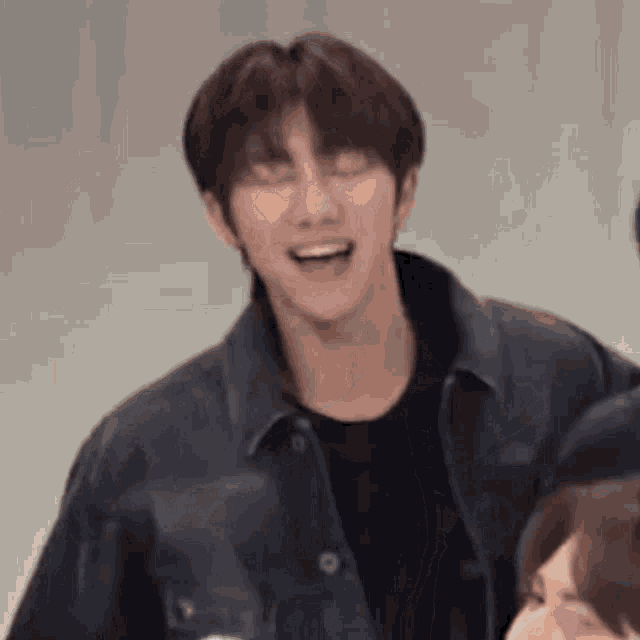 a man in a black jacket is laughing with his eyes closed and his mouth open .